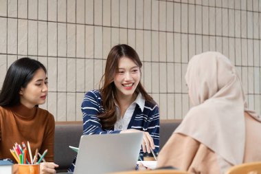 Üç öğrenci, öğrenim alanlarında öğrenme ve işbirliği üzerine yoğunlaşırken proje görevleri üzerinde beyin fırtınası yaparak tartışmaya giriştiler..