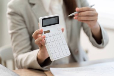 Finansal hesaplamaları tartışırken hesap makinesi gösteren bir iş kadını, kurumsal bir ortamda finansal yönetim becerilerini vurguladı.
