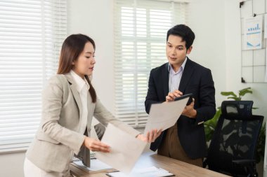 Bir kadın proje detaylarını tartışırken, şirket ortamında takım çalışması ve profesyonelliği vurgularken, bir erkeğe belgeler sunar..