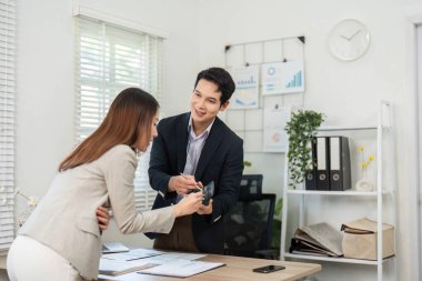 Bir kadın proje ayrıntılarını tartışırken, iş yerinde işbirliği ve iletişimi vurgularken, belgeleri bir erkeğe teslim eder.