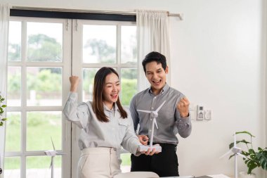 Bir erkek ve kadın, ESG ve yenilikçi iş uygulamalarına olan bağlılıklarını vurgulayan bir rüzgar türbini modelini hevesle tartışıyor..