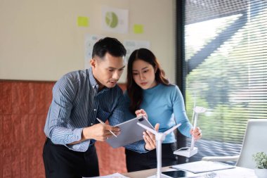 Bir ekip yenilenebilir enerji çözümlerini, bir rüzgar türbini modelini ve modern çalışma alanındaki tabletler üzerindeki dijital verileri analiz ederek tartışır..