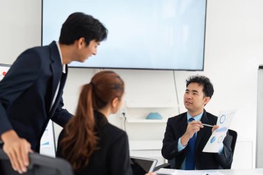 Üç meslektaşı proje verilerini tartışıyor ve modern ofis ortamında görüşleri paylaşıyor, takım çalışması ve iletişim sergiliyorlar.