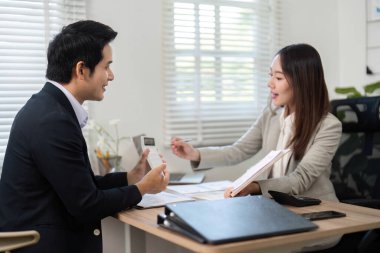 Bir mali danışman, modern ofis ortamında bir müşteriyle görüşür, belgeleri inceler ve mali yetkilendirme için yatırım seçeneklerini tartışır.