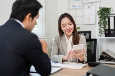 Bir müşteri, modern bir ofis ortamında finansal danışmanıyla birlikte akıllı telefondaki mali bilgileri incelerken gülümsüyor..