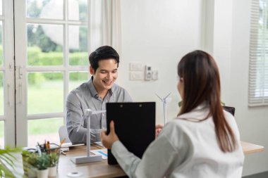 İki iş adamı ESG stratejileri, rüzgar türbini modellerinin sergilenmesi ve parlak bir ofiste sürdürülebilirlik planları hakkında bir tartışmaya girişti..