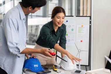 Yenilenebilir enerji projesi için tartışan ve ölçüm yapan iki mühendis, modern bir ofiste rüzgar enerjisi çözümlerine odaklanıyorlar..