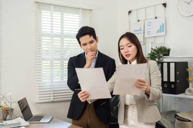 İki profesyonel proje belgelerini analiz eder, stratejileri ve görüşleri parlak, modern bir ofis alanında tartışırlar..
