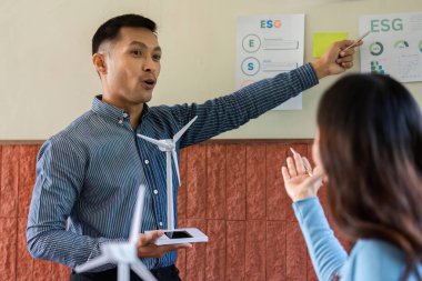 Bir erkek, yenilenebilir enerjideki ESG ilkelerini vurgulayan rüzgar türbini kavramlarını bir kadına tutkuyla sunar..