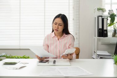 Ofisinde, bir kadın mali analizin zorluklarını sergiliyor, hesap makinesini kullanarak belgeleri incelikle inceliyor, problem çözme becerilerini vurguluyor..