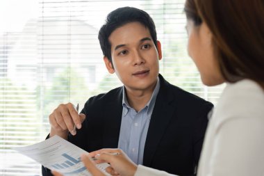 Bir danışma sırasında, profesyonel bir kişi bir müşteriyle finansal stratejileri tartışır, ayrıntılı raporlar ve görüşleri kullanarak sohbeti yönlendirmeye çalışır..