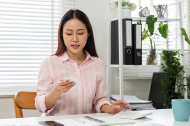 Genç bir kadın ev ofisinin etrafını sarmışken akıllı telefonuyla bilgilerini gözden geçirir..