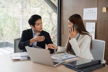 Profesyonel bir ortamda, bir erkek iş stratejilerini anlatırken kadın telefonuyla konuşur ve danışmada etkili bir iletişim olduğunu gösterir..