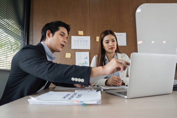 A man explains data insights to a woman as they analyze charts on a laptop, enhancing their decision-making in a corporate environment.