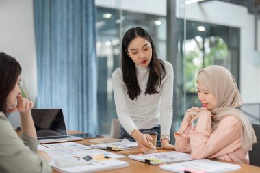 Modern bir ofiste üç kadın, dinamik bir toplantı sırasında fikir ve strateji alışverişinde bulunuyor..
