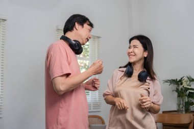 Orta yaşlı neşeli bir çift oturma odalarında kulaklık takıp birlikte gülüp dans ediyor ve sıcak bir ortamda özel bir anın tadını çıkarıyor..