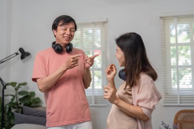 Çeşitli bir çift birlikte eğleniyor, kulaklık takmış, rahat bir oturma odasında dans ediyor ve gülümsüyor..