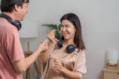 Birbirlerine eşlik eden, rahat bir oturma odasında dans eden ve gülümseyen, boyunlarına kulaklık takan farklı bir çift..