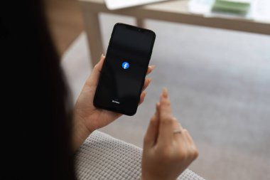 Facebook logosu olan bir akıllı telefonu tutan kişinin yakın plan fotoğrafı. Dijital iletişimi vurguluyor..