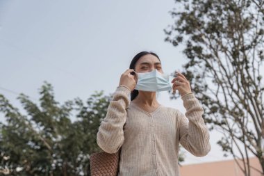 Genç bir kadın kamuya açık bir alanda koruyucu maskesini takarken gülümsüyor, pozitifliği ve sağlık bilincini arttırıyor..