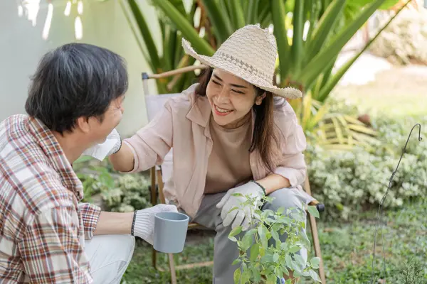 Yaşlı bir Asyalı çift bahçelerinde neşe dolu bir anı paylaşıyor. Kadın, partnerinin yüzüne şefkatle dokunuyor ve gülümsüyor..