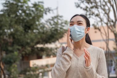 Genç bir kadın maske takarken gülümsüyor, kirlilik bilinci ve sağlık güvenliğinin önemine değiniyor.