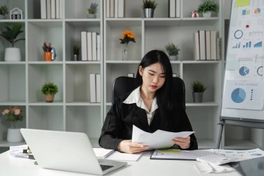 Bir kadın muhasebeci masasında oturuyor, mali raporları ve belgeleri inceliyor, modern bir ofiste vergi dosyasına hazırlanıyor..