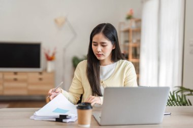 Evrakları inceleyen ve bilgisayarını rahat bir ofiste çalışırken notlar alan odaklanmış genç bir kadın verimli bir atmosferi vurguladı..