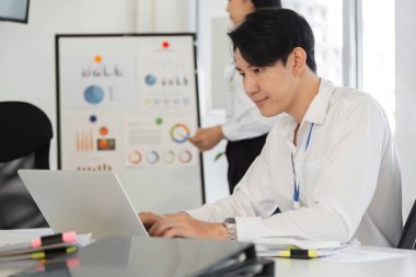 İşbirlikçi bir ofis ortamında veri tablolarını analiz ederken bilgisayarına kendini adamış bir adam yazı yazar..