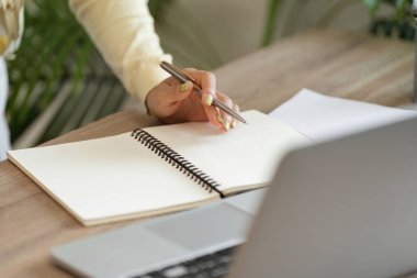 Bir kadın, ofis masasında çalışırken not defterine not alır. Organizasyonu ve odaklanmayı önemser..