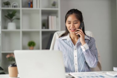 Bir telefon görüşmesi sırasında finansman uzmanı gülümsemesi, modern ofis ortamında onun nişanını ve profesyonelliğini vurguluyor..