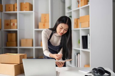 Bir e-ticaret işkadını nakliye etiketleri hazırlıyor ve paketlerle dolu modern bir ofiste masasında siparişleri gözden geçiriyor..