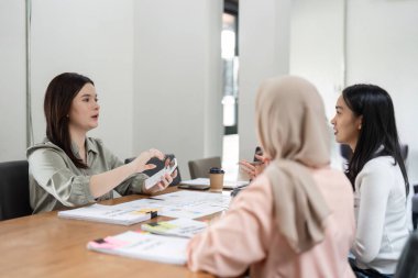 Çeşitli bir grup kadın, mali raporları ve stratejileri coşkuyla tartışan, ortak bir ofis toplantısına katılıyor..