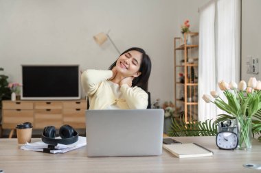 Genç bir kadın masasında otururken nazikçe boynuna masaj yapıyor. Ev ortamında kendine bakmanın önemini gösteriyor..