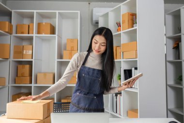 Genç bir kadın, envanteri verimli bir şekilde yönetmek için bir defter kullanarak, modern bir çalışma alanında paketler düzenler..