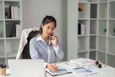 Kendini işine adamış bir finans işçisi, bir telefon görüşmesinde mesleki bir ortamda birden fazla görev içeren çizelgeleri ve verileri gözden geçirir..