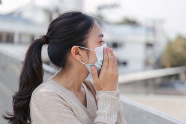 Genç bir kadın hava kalitesi ve kirliliğinden endişe ederken doğanın tadını çıkararak maskesini açık havada ayarlıyor..