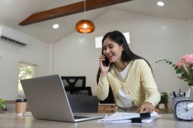 Bir iş kadını dizüstü bilgisayarı üzerinde çalışırken bir telefon görüşmesi yapar ve evdeki belgeleri gözden geçirir..