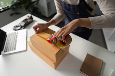 İyi organize edilmiş bir çalışma alanında paketleri bantlayan bir kadının yakın plan görüntüsü detaylara ve verimliliğe olan ilgisini vurguluyor..