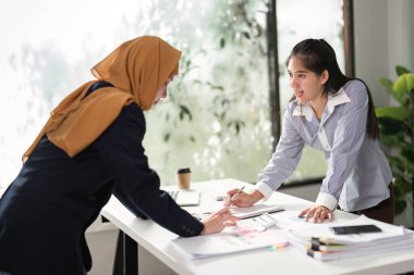 Parlak bir ofis ortamında raporları ve stratejileri tartışan iki kadın mali analizde işbirliği yapıyor..
