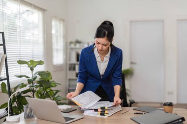 Profesyonel bir muhasebeci, vergi belgelerini masasında inceleyip finansal organizasyonun önemini ve detaylara dikkat çeker..