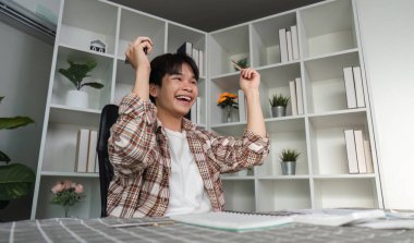 Finansal başarısını sevinçle kutlayan genç bir adam, elinde nakit para ve kağıtlar tutarak, finansal başarısını vurguladı..