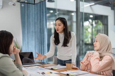 Bir grup farklı kadın, çağdaş bir ofis ortamında üretken bir toplantıya katılıyor, fikirleri ve stratejileri paylaşıyor..
