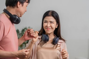 Olgun bir çift, evde kulaklık takıp neşeyle dans ediyor ve gülümsüyor, birlikte eğlenceli ve sevgi dolu bir anın tadını çıkarıyor..