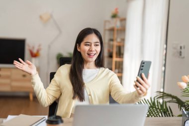 Heyecanlı genç bir kadın telefonunu sıcak bir ofiste tutarken bir video görüşmesine katılıyor. Hevesli ve arkadaş canlısı bir tavır sergiliyor..