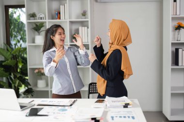 İki farklı iş kadını modern bir ofiste heyecan paylaşıyor, takım çalışmalarını ve son zamanlardaki başarılarını kutluyorlar..
