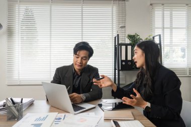 Verileri analiz eden ve iyi aydınlatılmış modern bir ofiste finansal stratejiler hakkında bir tartışmaya giren iki farklı profesyonel.