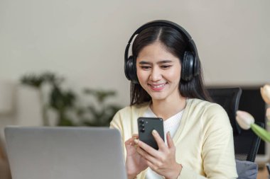 Neşeli bir iş kadını evde akıllı telefonunu kullanarak teknolojinin ve serbest çalışmanın karışımını resmederken gülümsüyor..