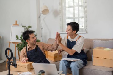 İki online satıcı fikirlerini paylaşıyor ve takım çalışmalarını paketlerle dolu şık bir evde ve bir dizüstü bilgisayarla kutluyorlar..