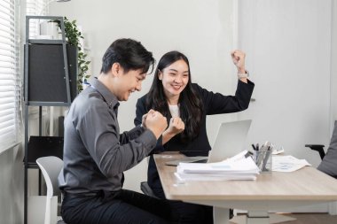 Bir ofis ortamında dizüstü bilgisayar üzerinde çalışırken, çeşitli iş ortaklarından oluşan bir ekip başarılarını neşeli ifadelerle kutluyor..